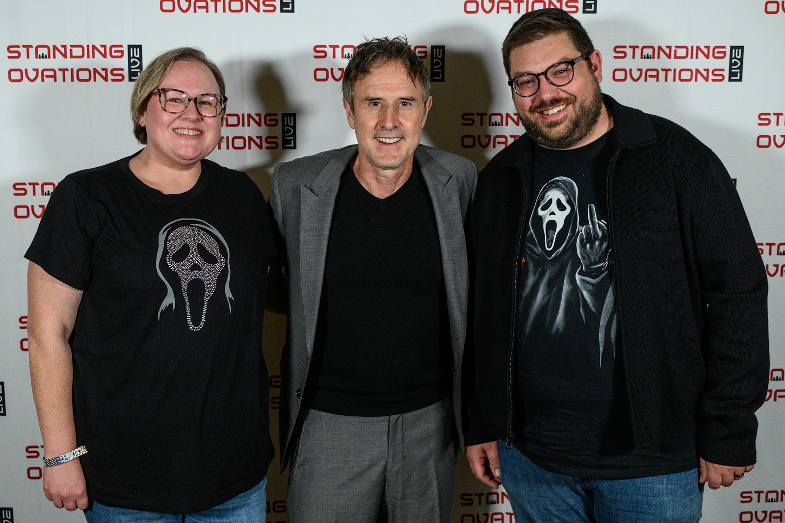 Three people in front of a Standing Ovations backdrop, two of them in Ghostface t-shirts.