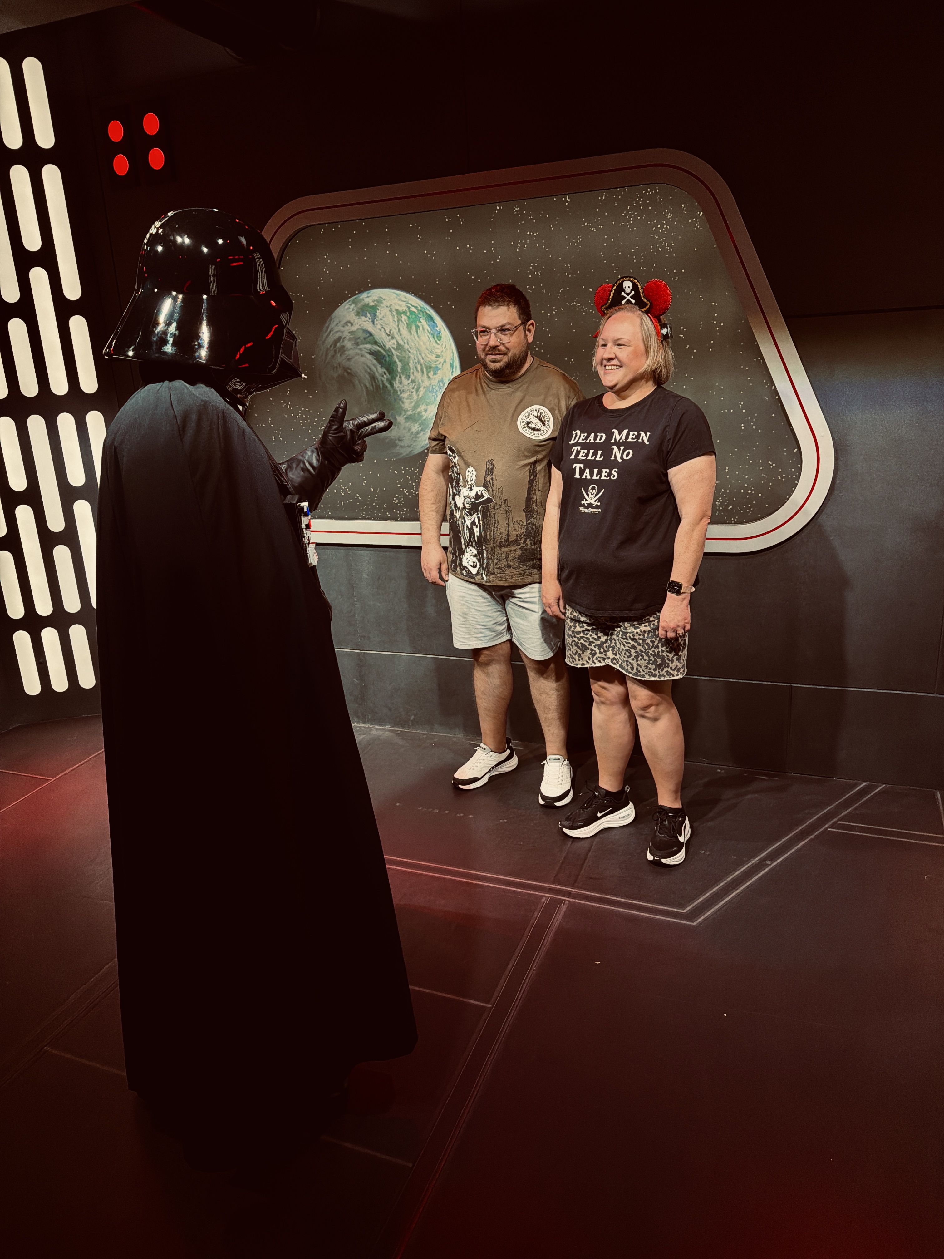 Two guests posing on a Star Wars set while Darth Vader gestures at them.
