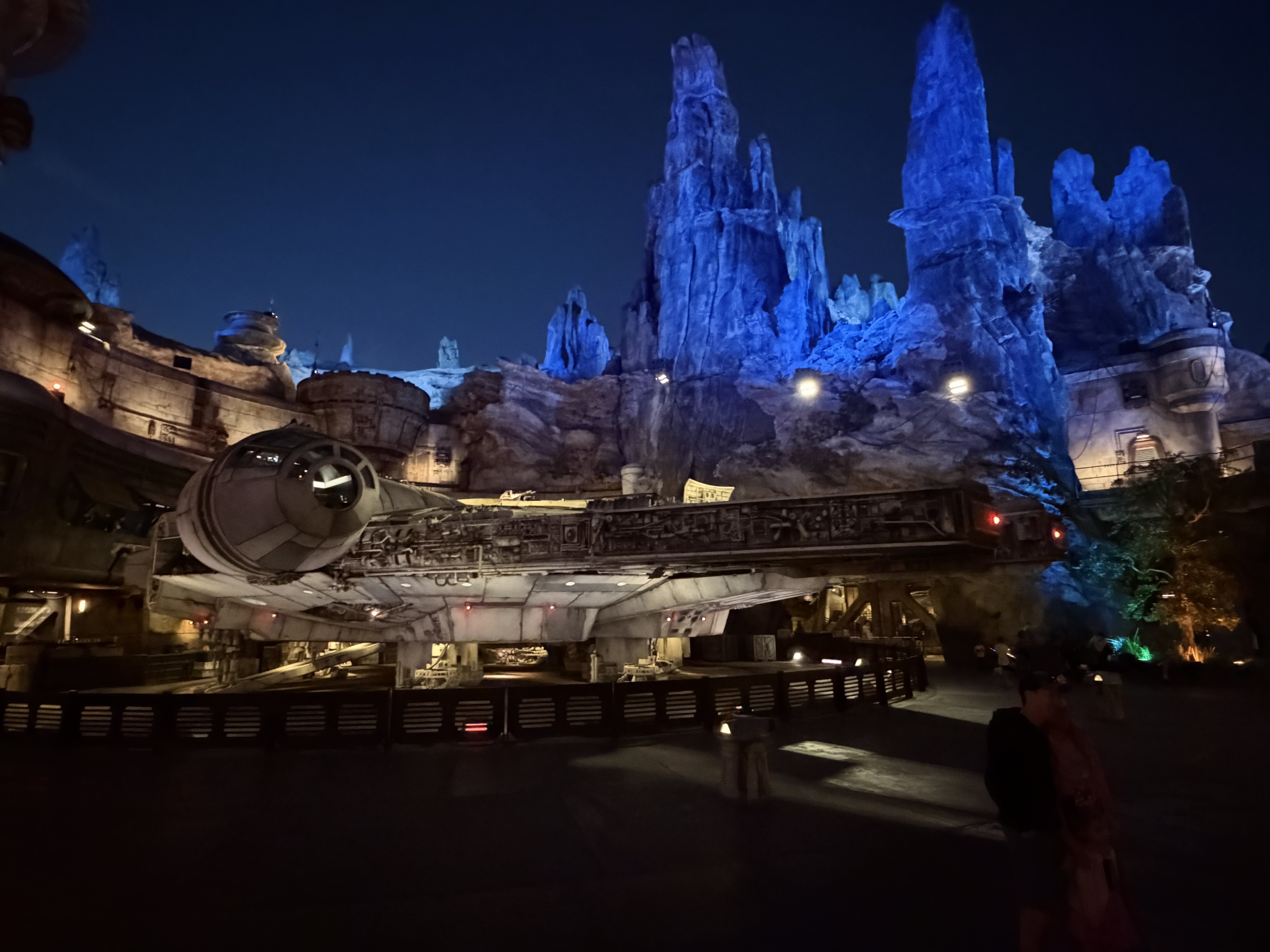 The Millennium Falcon under blue-lit rock spires at night.