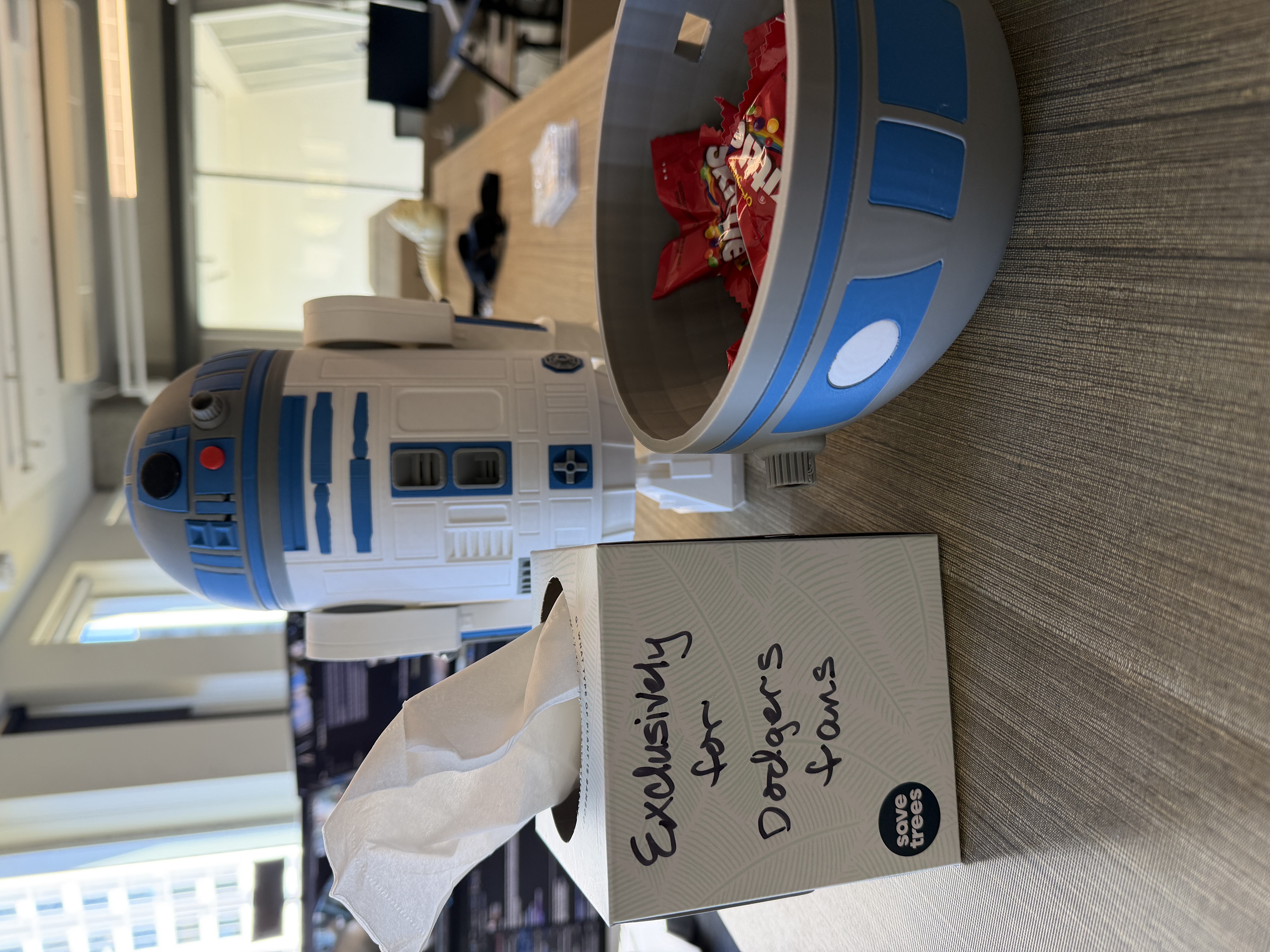 A desk "support station": an R2-D2 figure, a tissue box labelled "Exclusively for Dodgers fans" and a bowl of candy.